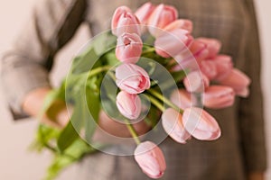 Young woman holding a beautiful bunch of tulips in her hands. Spring present for a girl in a grey dress. Flowers bouquet