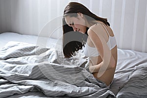 Young woman holding belly sitting in bed suffering from pain during menstruation