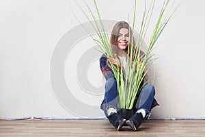 Young woman holding big green plant sitting against wall.