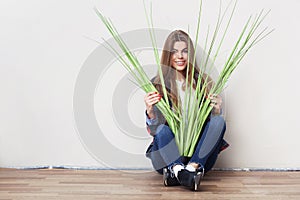 Young woman holding big green plant sitting against wall.