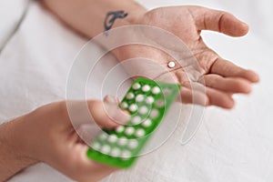 Young woman holding birth control pills at bedroom