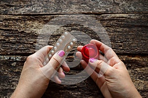 Young woman holding a birth control pills and a condom on wooden background