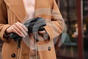 Young woman holding black leather gloves, closeup. Stylish clothes