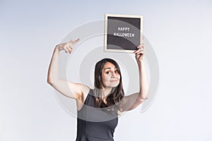 young woman holding a black vintage letter board with happy halloween sign. White background. LIfestyle indoors