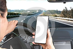 Young woman holding blank screen cell phone while driving car. Mockup phone. Car is speeding along the highway