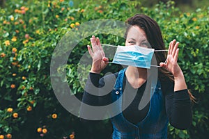 Young woman holding a blue medical mask in her face by hands on blurred green background.