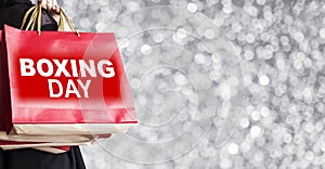 Young woman holding boxing day shopping bag on silver bokeh