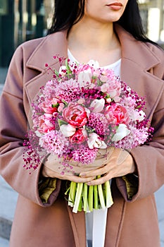 Young woman holding bridal bouquet in pink lilac tones made of hyacinth, tulips and gypsophila
