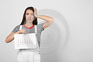 Young woman holding calendar with marked menstrual cycle days on light background. Space for text