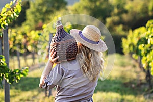 Young woman holding carboy with wine in vineyard