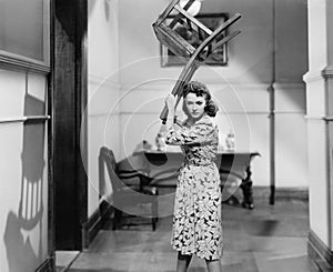 Young woman holding a chair above her head in anger