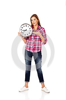 Young woman holding clock and pointing for it