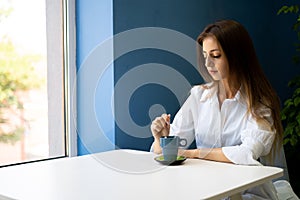 Young woman holding coffee spoon and stirring hot coffee on white table at cafe.