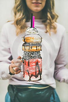 Young woman holding cold strawberry donut freakshake in mason jar