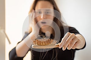 Young woman holding a comb with a lock of hair in front of her, focus on comb, hair loss problem
