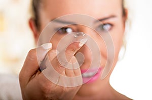 Young woman holding contact lens on finger in front of her face on white background., eyesight and eyecare concept photo