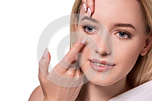 Young woman holding contact lens on index finger with copy space. Close up face of healthy beautiful woman about to wear