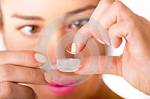 Young woman holding contact lenses cases and lens in front of her face