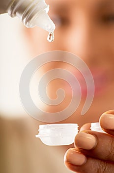 Young woman holding contact lenses cases and lens in front of her face