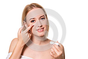 Young woman holding contact lenses cases and lens in front of her face on white background