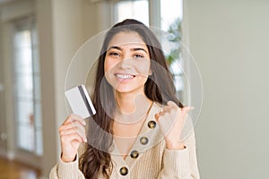 Young woman holding credit card as payment pointing and showing with thumb up to the side with happy face smiling