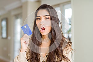 Young woman holding credit card as payment scared in shock with a surprise face, afraid and excited with fear expression