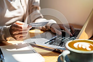 Young woman holding a credit card and using computer for making online payment shopping at coffee shop