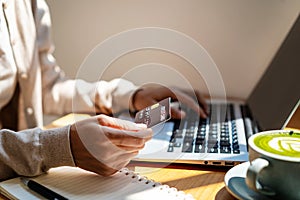 Young woman holding a credit card and using computer for making online payment shopping at coffee shop