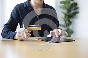 Young woman holding credit card and using digital tablet for paying bills online or shopping online.