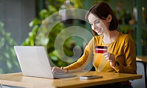 Young woman holding credit card and using laptop at cafe