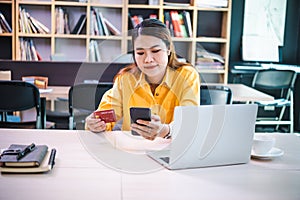 Young woman holding credit card and using laptop computer. Businesswoman working at cafe. Online shopping, e-commerce, internet