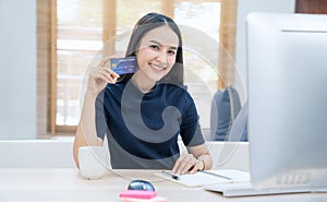 Young woman holding credit card and using laptop computer. Businesswoman working at home. Online shopping, E-commerce, internet ba