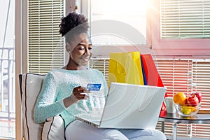Young woman holding credit card and using laptop computer. Online shopping concept. Happy black woman doing online shopping at