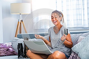 Young woman holding credit card and using laptop computer. Online shopping concept. Happy woman doing online shopping at home