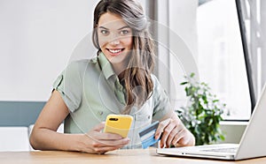 Young woman holding credit card, using laptop computer and smartphone at home. Businesswoman or entrepreneur working