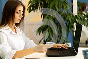 Young woman holding a credit card and using a laptop making an online payment in the office. Online shopping