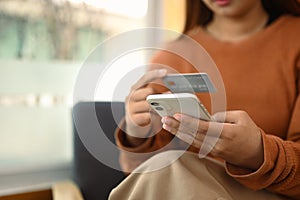 Young woman holding credit card and using mobile phone. Banking transaction and shopping online concept