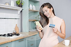 Young woman holding credit card and using smart phone at home. Online shopping, spending money, enjoying life concept