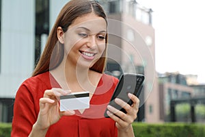 Young woman holding credit card and using smart phone. Online shopping, e-commerce, internet banking, spending money, working from