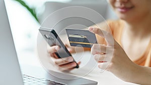 Young woman holding credit card and using smartphone for online shopping, internet banking, e-commerce, spending money, working
