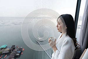 Young woman holding cup, looking sea view in raining morning