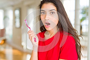 Young woman holding dental toothbrush scared in shock with a surprise face, afraid and excited with fear expression