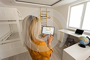 young woman holding digital tablet with black empty screen for mockup template, standing at modern kitchen. Technology