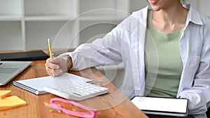 Young woman holding digital tablet and writing information on notepad.