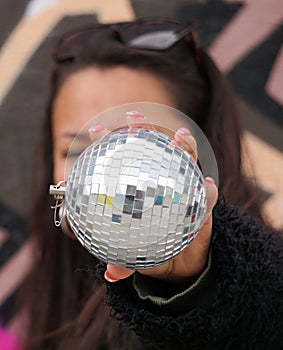 A young woman holding a disco ball in front of her face