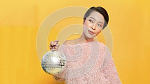 Young woman holding disco ball while standing on yellow