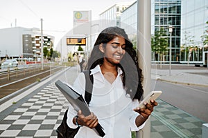 Young woman holding document folder and cellphone while walking on street