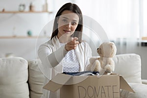 Young woman holding donation box, pointing finger at you