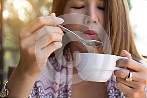 Young woman holding drinking coffee using spoon blowing hot coffee before drinking in the morning at home..Asian girl drinking