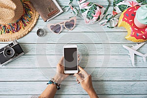 Young woman holding empty screen smart phone with travel summer accessories and items on wooden background with copy space